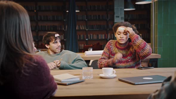 Mixed Race Group of Friends Playing Guessing Game at Library alt