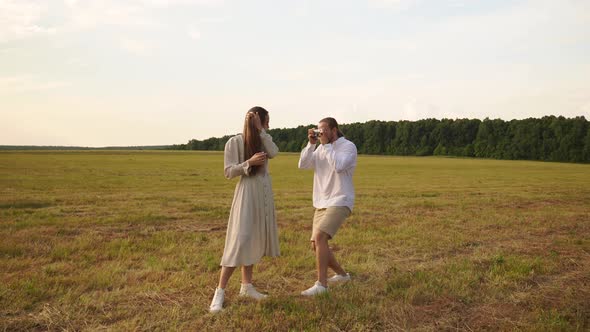 A Man Photographs a Woman on a Film Camera in a Field at Sunset