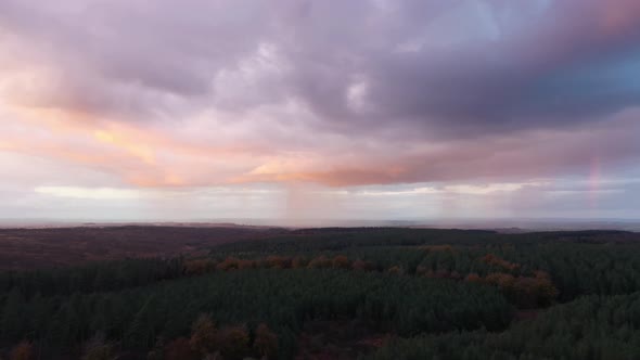 Woodland at sunset with storm clouds, rain and rainbow in the distance backgr