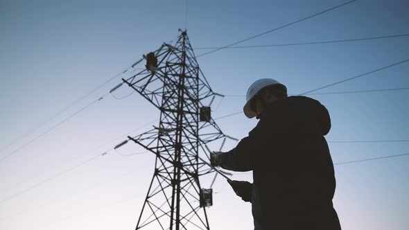 A Construction Engineer Power Engineer in a Protective Helmet Checks the Poles of Power Lines alt