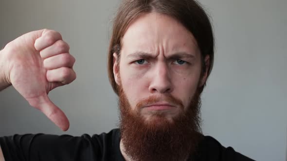 Young Handsome Man with Beard Expressing Discontent and Showing Thumb Down