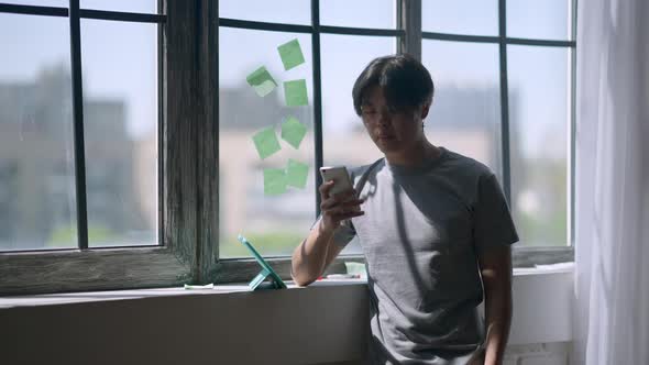 Asian Young Man Dialing Number on Smartphone Calling Business Partner From Home Office alt