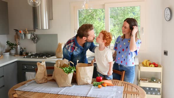 Family unpacking groceries and kissing each other in kitchen alt