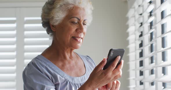 African american senior woman using smartphone and looking out of the window at home alt