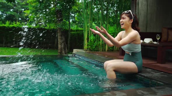 slow-motion of woman sitting on edge of swimming pool and playing water splashing