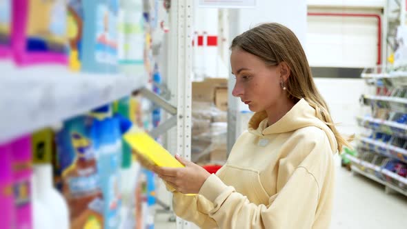 Woman Choosing Detergent at a Household Goods in the Store alt