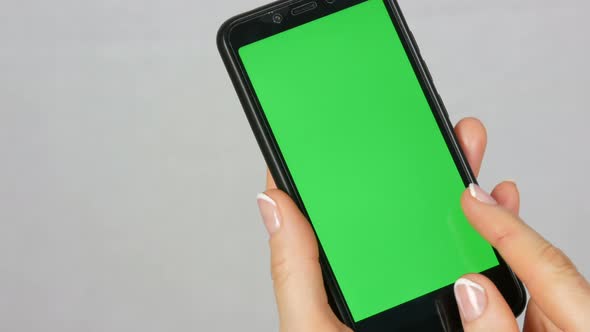 Wellgroomed Neat Female Hands with a Beautiful Manicure Hold a Black Smartphone with a Green Screen alt