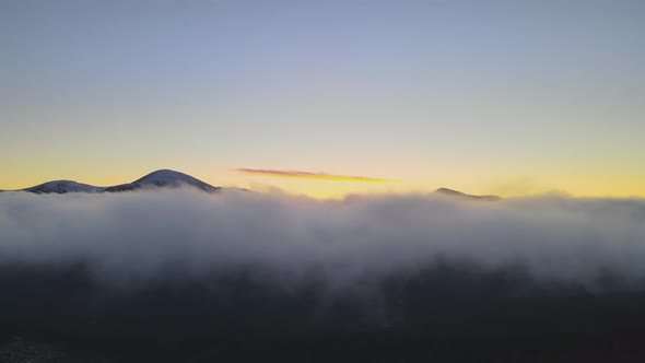 Aerial view of vibrant sunrise over white dense fog with distant dark peaks of Carpathian alt