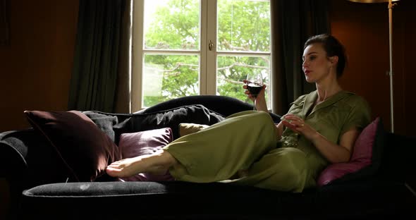 Woman with glass of wine sits down in sofa. Boudoir scene, slider shot alt