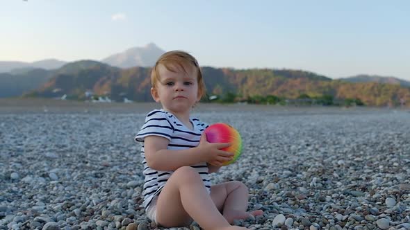 Cute little baby girl with colorful ball in hands sitting on a beach