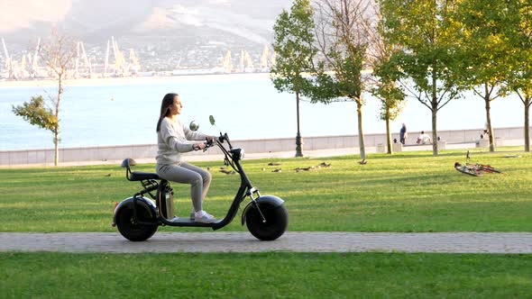Young girl on electric scooter is riding through public park at sunny morning