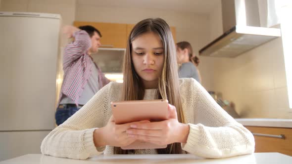 Young Girl Using Tablet Computer and Ignoring Arguing and Shouting Parents alt