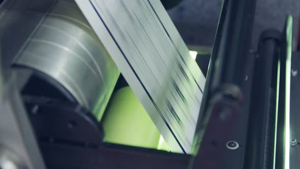 Closeup on paper moving through a large industrial printing machine alt