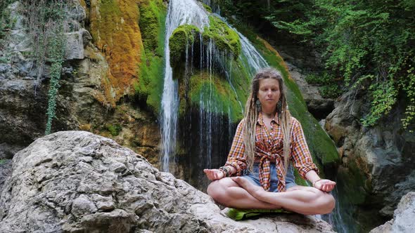 Girl Sits in Padmasana on Stone Near Waterfall alt