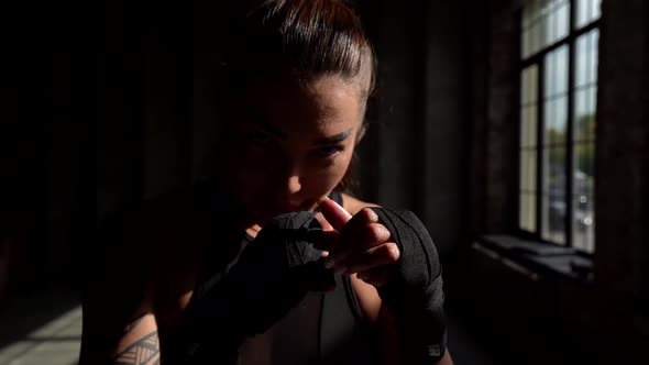 Close-up of a Young Attractive Female Boxer in Armbands Stands in a Spectacular Pose and Looks at alt