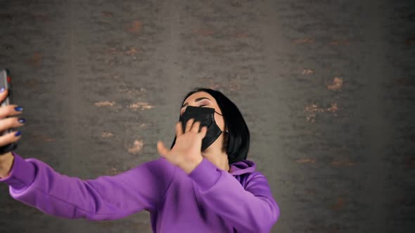 Cheerful Young Brunette Woman Takes Selfie in Black Face Mask Using Smartphone alt