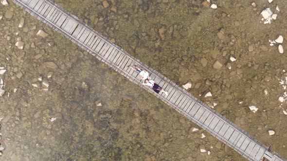 Aerial Top Down View of Young Couple in Love Lying Together on Wooden Bridge Over River alt