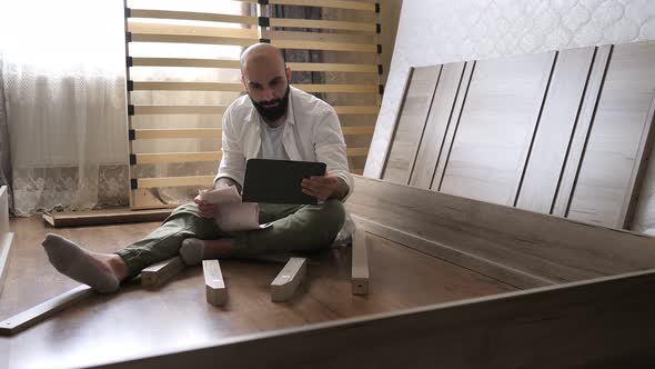 Bearded Man with Tattoo on the Hand with Instruction in the Tablet for Assembling Furniture is Going