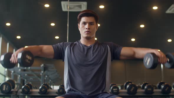 Young athlete Asian guy exercising doing lifting dumbbell fat burning workout in fitness class.