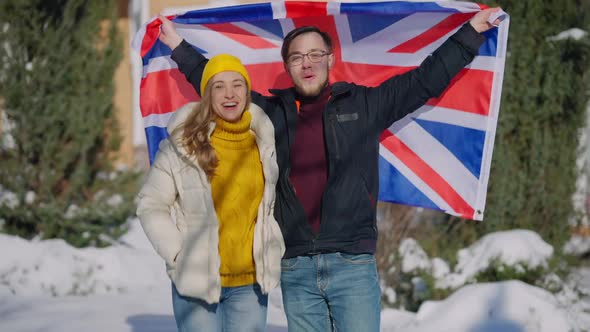 Medium Shot of Happy Couple Posing with British Flag Outdoors on Sunny Winter Day alt