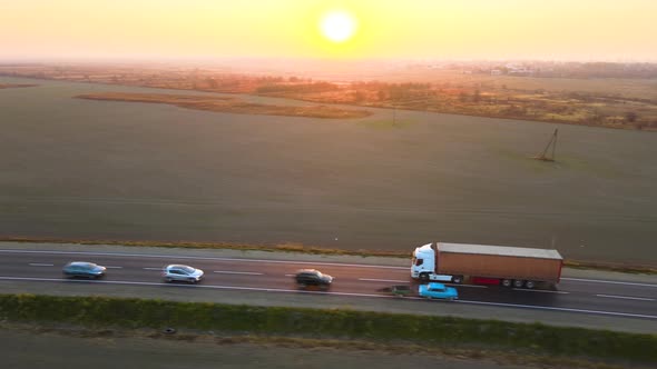 Aerial View of Semitruck with Cargo Trailer Driving on Highway Hauling Goods in Evening alt