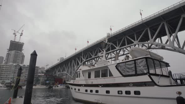 Yacht anchored in Granville island dock under bridge on cloudy day alt