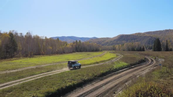 a car drives on a rural road around a field, a forest against a background of a mountain