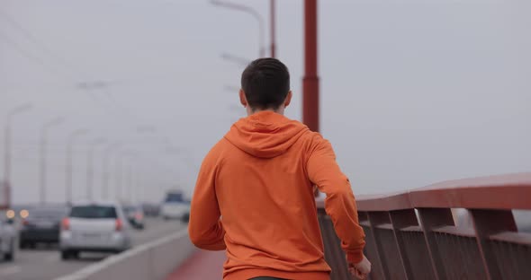 Man in Orange Hoodie Running on a Bridge Back View alt