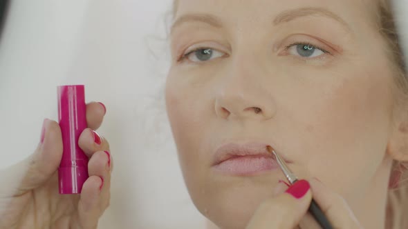 hands of makeup artist apply lipstick with brush on lips