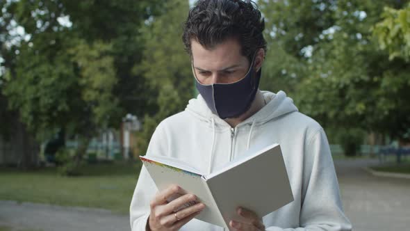 Slow Motion of Handsome European Man in Face Mask Standing in City Park and Reading Notes in alt