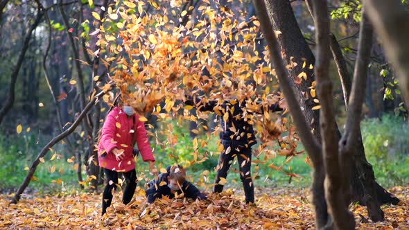 Small Children in Medical Masks Throw Fallen Yellow Leaves in the Park on an Autumn Day