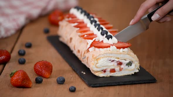 Close up, young girl is cutting meringue roulade with berries and mascarpone alt