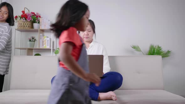 Calm mother sit on couch working on laptop, little kids play around, peaceful mom relax on sofa alt