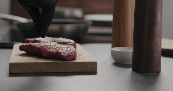 Slow Motion Orbit Shot of Man Salting Raw Beef Steak on Oak Board alt