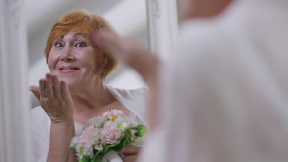 Reflection in Mirror of Confident Happy Senior Bride Gesturing Air Kiss in Slow Motion Smiling alt
