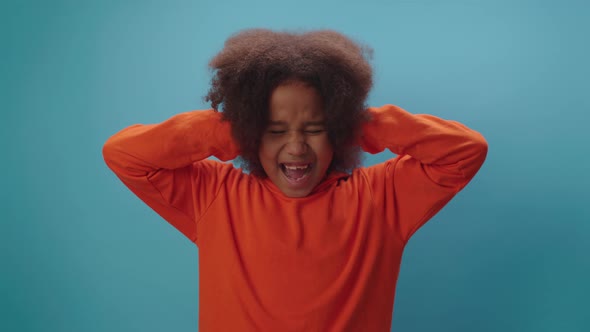 Cute African American girl with closed eyes and ears shouting NO standing on blue background. alt