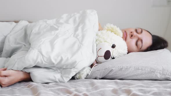 Young Woman Goes to Sleep with Teddy Bear in Her Bedroom alt
