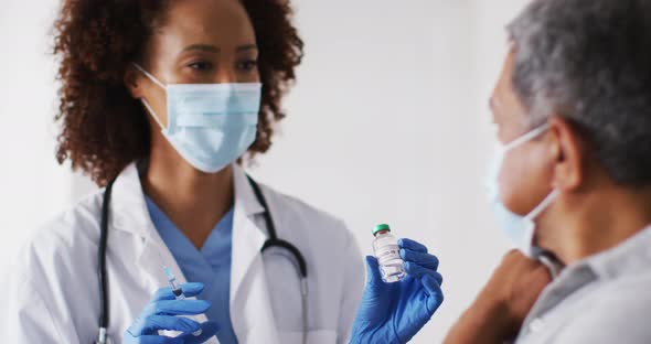 Mixed race female doctor wearing mask giving vaccination to senior man at home alt