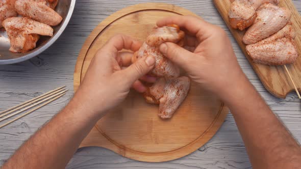 The Top View of the Male Hands Piercing Chicken Wings with a Wooden Skewer alt