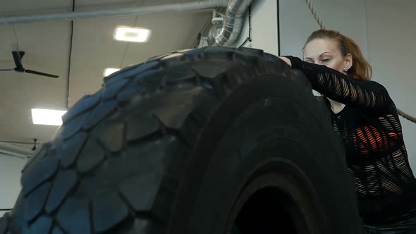 Caucasian athlete woman rolls big tires in the gym. Young woman exercising crossfit