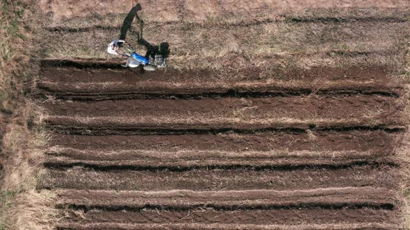 AERIAL - Man working a field with a rototiller, agriculture, wide shot tilt up alt