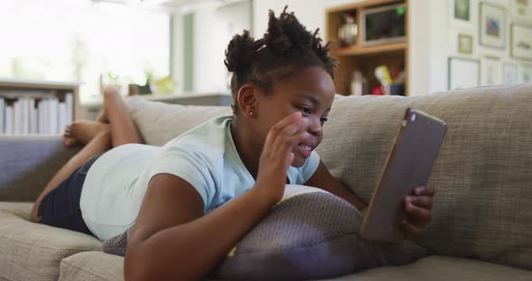 Happy african american girl lying on sofa using tablet alt