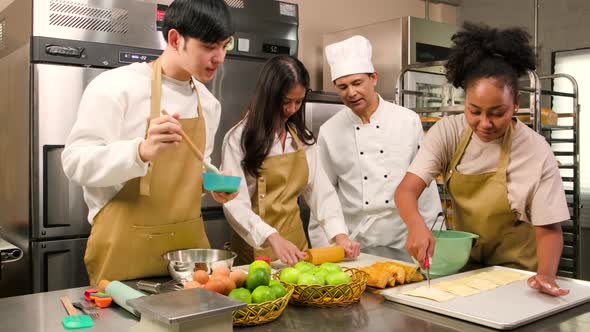 Senior male chef teaches cooking students to prepare ingredients for fruit pies.