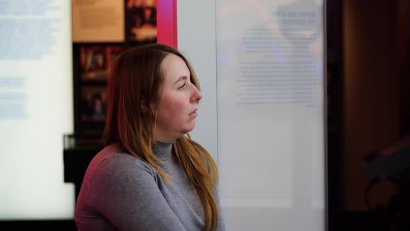 Beautiful woman is waiting for someone standing at advertising stand in Museum alt