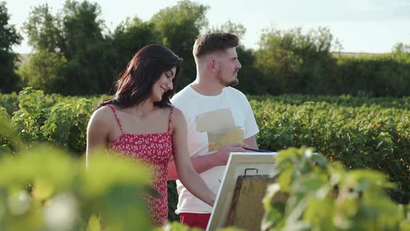Portrait of Artists' Couple Talking and Smiling During Painting in Green Field alt