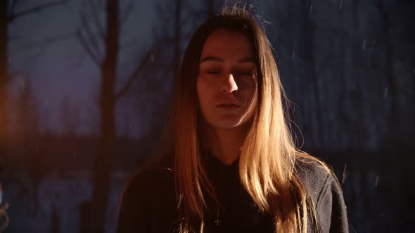 Young Woman with Torch Standing in Winter Forest Under the Snowfall and Looking in the Camera alt