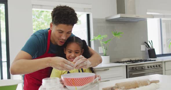 Happy biracial father and daughter baking together in kitchen alt
