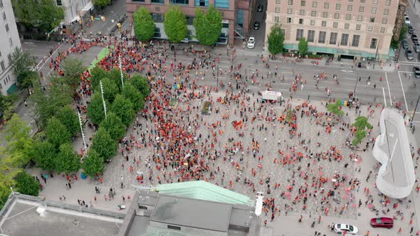 Huge crowd of protesters assemble below, orbiting aerial view from above in UHD alt