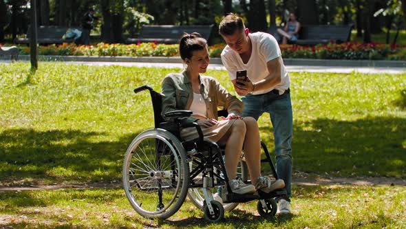 Woman in a Wheelchair and Her Friend Spending Time at the Summer Park and Taking a Selfie on the alt