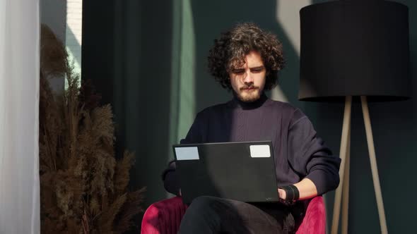 Man Sitting Near Window and Working at the Laptop at the Sunset Admiring the View alt